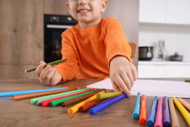 Mutfaktaki masasında keçeli kalemlerle çizen sevimli küçük çocuk.