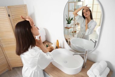 Banyoda aynanın yanında yüz geliştirme egzersizi yapan genç bir kadın.