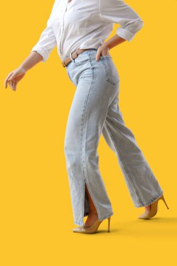 Sarı arka planda yürüyen kotlu şık genç kadın.