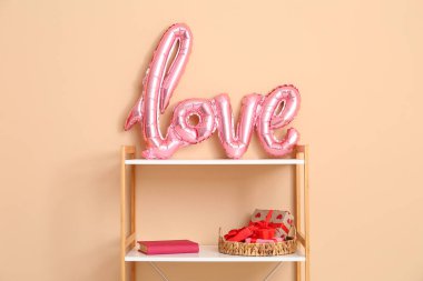 İçinde balonlardan ve bej duvarın yanındaki hediye kutularından yapılmış aşk sözcüğü olan kitaplık. Sevgililer Günü kutlaması
