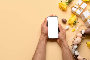 Modern cep telefonlu erkek eller, hediyeler ve renkli arka planda Paskalya dekoru.