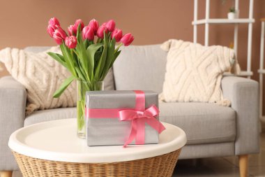 Çiçekli vazo ve hediye paketi oturma odasındaki sehpanın üzerinde.