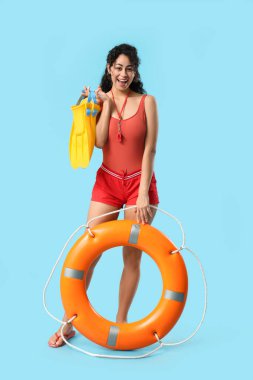 Mavi arka planda yüzgeçleri ve yüzük şamandırası olan güzel, mutlu, Afro-Amerikan bayan cankurtaran.