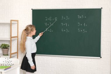 Sınıfta ders sırasında tahtaya işaret eden sevimli bir kız.