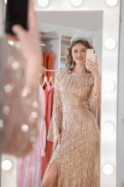 Güzel, genç ve mutlu bir kadın balo gecesine hazırlanıyor ve dolabın önünde aynada fotoğraf çekiyor.
