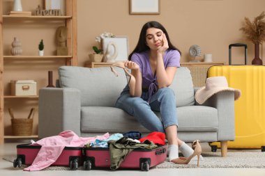 Oturma odasındaki bavulların yanındaki koltukta oturan düşünceli genç bayan.