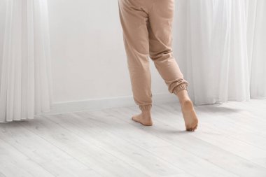 Çıplak ayaklı kadın, odada, arka planda, lamine zeminde yürüyor.