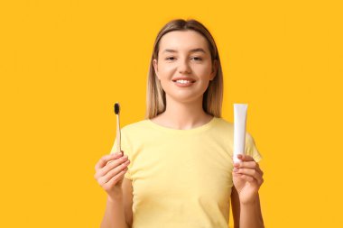 Sarı arka planda diş fırçası ve yapıştırıcısı olan genç bir kadın.