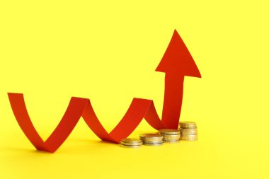 Sarı arka planda bozuk paralarla kırmızı ok. Fiyat artışı kavramı