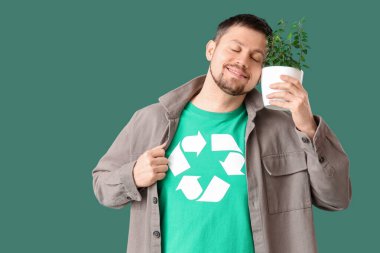 Geri dönüşüm logosu ve yeşil arka planda bitki yetiştiren tişörtlü mutlu genç adam. Ekoloji kavramı