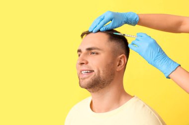 Sarı arka planda saç büyümesi için iğne yapılan mutlu genç adam, yakın plan.