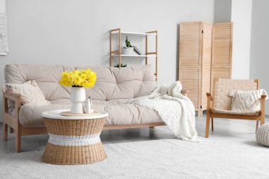 Şık bir oturma odası. Kanepesi, narsisli çiçekleri ve kahve masası var.