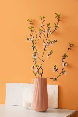 Turuncu duvarın yanındaki masada çiçek açan dalları olan vazo, yakın plan.
