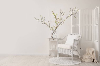 Koltuklu hafif oturma odası, kahve masası ve çiçek açan dalları olan vazo.