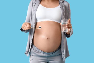 Diş fırçası ve mavi arka planda bir bardak su olan hamile bir kadın.