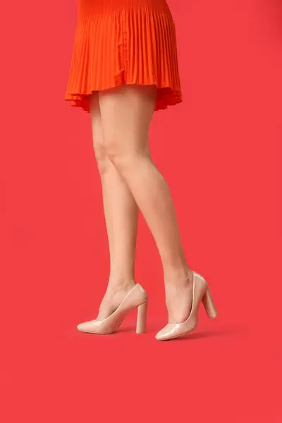 Legs of young woman in stylish beige high heels on red background
