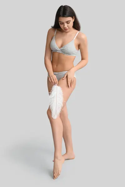 灰色の背景に柔らかい羽を持つ美しい若い女性 エピレーションコンセプト — ストック写真