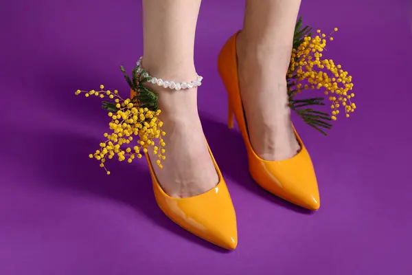 Ноги Красивой Молодой Женщины Оранжевых Каблуках Мимозой Фиолетовом Фоне — стоковое фото