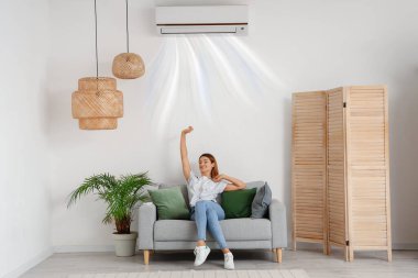 Klimalı genç bir kadın evdeki kanepede oturuyor.