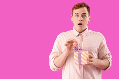 Şok olmuş genç kızıl saçlı adam mor arka planda hediye kutusuyla