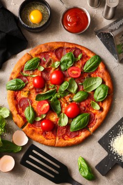 Domatesli ve arka planda fesleğenli lezzetli Pepperoni pizzası.