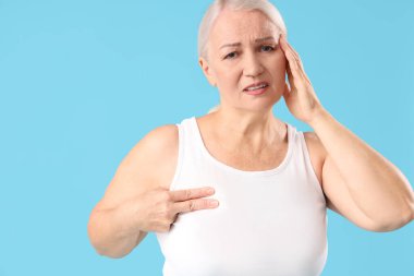 Mavi arka planda göğüs ağrısı çeken olgun bir kadın. Kanser farkındalığı kavramı