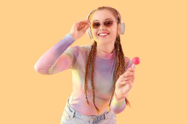 Güzel, genç ve mutlu bir kadın. Güneş gözlüklü ve lolipoplu. Renkli arka planda müzik dinliyor.