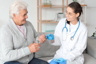 Yaşlı adam evde hemşireden hap alıyor.