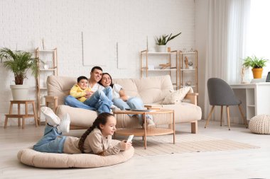 Ailesi evde televizyon izlerken cep telefonu kullanan küçük bir kız.