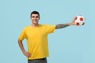 Mavi arka planda futbol topu olan mutlu genç adam.