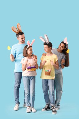 Mavi arka planda Paskalya yumurtaları olan tavşan kulaklı mutlu bir aile.