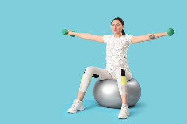 Güzel, genç, hamile bir kadın, spor yapıyor ve mavi arka planda dambıllar var.