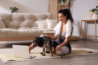 Sportif, Afro-Amerikalı, cocker spaniel köpeği olan genç bir kadın evde antrenmandan sonra oturuyor.