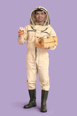 Male beekeeper with box of honey on lilac background clipart