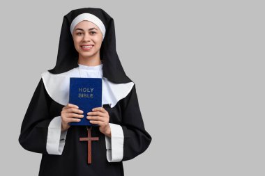 Gri arka planda İncil 'i olan genç rahibenin portresi