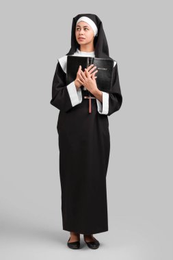 Gri arka planda İncil 'i olan genç rahibenin portresi