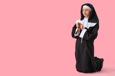 Young nun with beads praying on pink background clipart