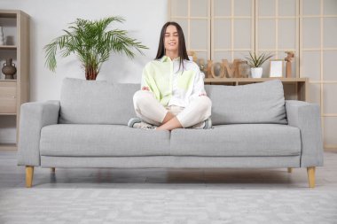 Gri kanepede meditasyon yapan güzel bir kadın.