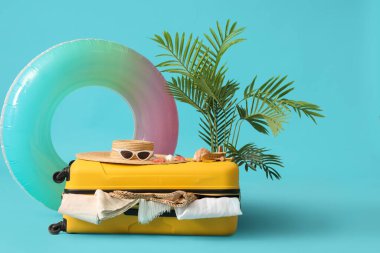 Plaj aksesuarlarıyla dolu bavul, egzotik bitki ve renkli arka planda şişme yüzük.