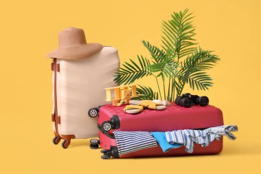 Kumsal aksesuarları, giysileri ve sarı arka planda egzotik bitkileri olan bavullar.