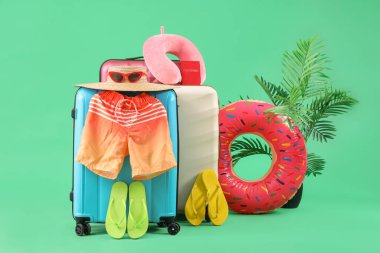 Plaj aksesuarlı bavullar, pasaport ve yeşil arka planda egzotik bitkiler.