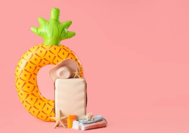 Bavul, plaj aksesuarları, şişirilebilir yüzük ve pembe arka planda dekor.