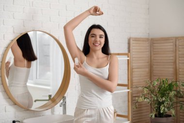 Mutlu gülümseyen genç kadın banyoda kristal deodorant kullanıyor.