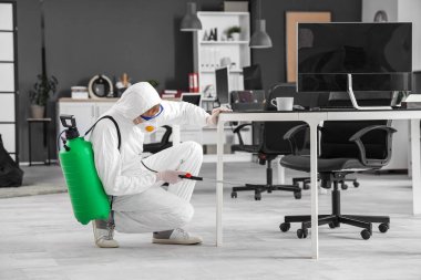 Erkek işçi ofiste masanın altında dezenfekte ediyor.