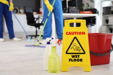 Ofis zemininde deterjan şişeleri ve kova olan uyarı levhası, yakın çekim.