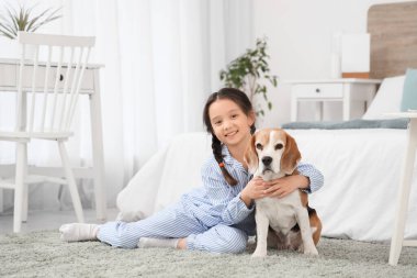 Küçük tatlı Asyalı kız yatak odasında Beagle köpeğine sarılıyor.