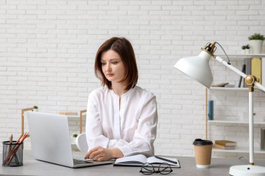 Genç iş kadını modern dizüstü bilgisayarla şık bir ofiste masada oturuyor.