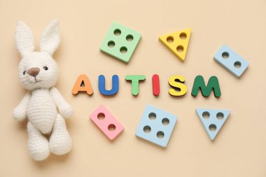 Kelime AUTISM, eğitici oyuncaklar ve bej arka planda tavşan. Üst görünüm