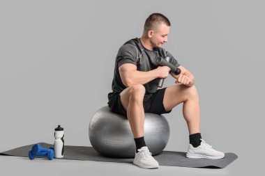 Genç bir adam hafif arka planda vurmalı masaj aleti ile koluna masaj yapıyor.