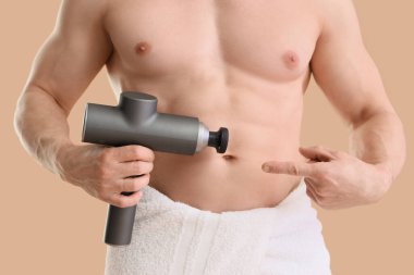 Bej arka planda vurmalı masaj aletini gösteren kaslı genç adam, yakın plan.